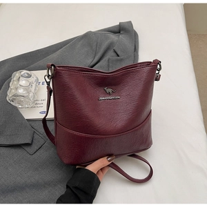 Detail of burgundy crossbody bag with litchi texture and kangaroo logo on grey blazer