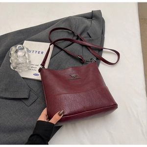 Detail of burgundy leather shoulder bag with lychee texture and kangaroo logo on grey suit