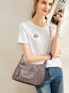 Detail of dark brown leather crossbody bag with multiple zip pockets and silver logo