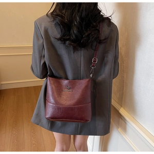 Detail of burgundy lychee grain leather crossbody bag with a gold kangaroo logo charm