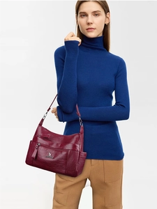 Deep burgundy leather crossbody bag with kangaroo logo shown on a blue sweater model