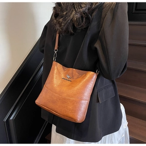 Brown bucket bag with pebble leather texture and golden kangaroo logo worn by a model