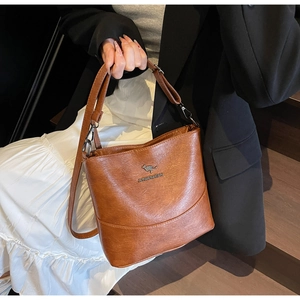 Detail of a brown bucket bag with a silver kangaroo logo and adjustable leather strap