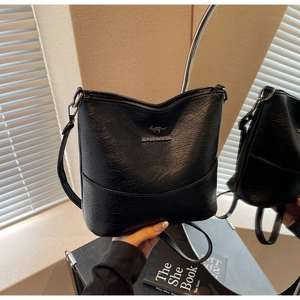Macro detail of black leather bucket bag with metal kangaroo logo on wooden surface