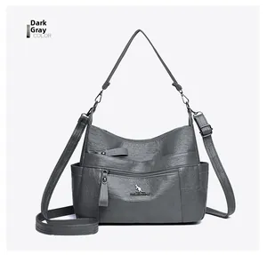 Detail view of dark gray crossbody bag with smooth faux leather texture and metallic logo