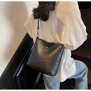 Detail view of a black textured leather tote bag with a golden kangaroo logo on a model
