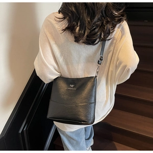 Detail view of the silver kangaroo logo on a black leather bucket bag worn on shoulder