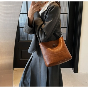 Close-up of brown PU leather bucket bag with golden kangaroo emblem on a female model