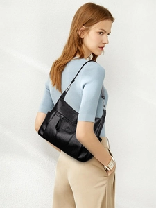 Detail of black glossy crossbody bag with adjustable strap and front zipper pocket