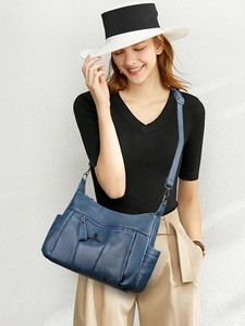 Close-up of blue leather crossbody bag with kangaroo logo and side pockets worn by a model