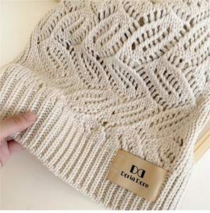 Close-up of cable knit texture on soft warm knitted beanie with leather brand label