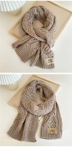 Detail of light beige cable knit scarf with thick wool texture and leather brand label