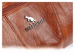 Detail shot of brown leather texture and silver kangaroo logo on crossbody bag