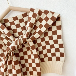Brown and beige checkerboard knit shawl with ribbed edges shown on a wooden hanger