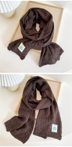 Detail of dark brown knit scarf showing hollow diamond pattern and white brand label