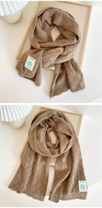 Close-up of brown knitted scarf with hollow patterns and brand label on wooden frame