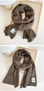 Close-up of tan chunky knit scarf showing textured cable stitch and detailed brand tag