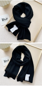 Detail of black knit scarf showing fine texture, stitching, and white care label