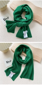 Close-up of green ribbed knit scarf texture with quality wash label and wooden tray