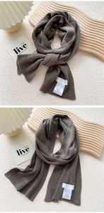 Detail view of grey knit scarf with fine texture and white care label on wooden board