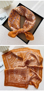 Detail view of burnt orange silk square scarf with geometric patterns in a black gift box