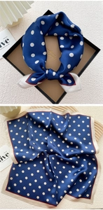 Detailed view of navy polka dot silk scarf with elegant borders inside a premium gift box
