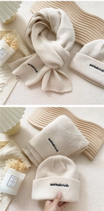 Detail of cream knit beanie and scarf set with black letter embroidery on wood background