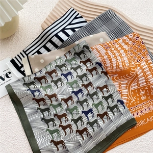 Collection of silk square scarves featuring horse prints and geometric patterns on a tray