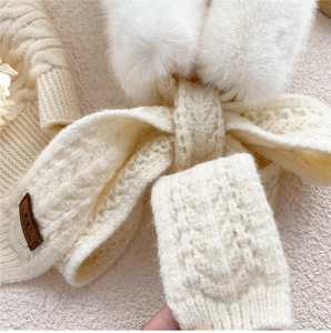 Detail of cream cable knit scarf featuring soft faux fur pompom and leather brand tag