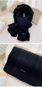 Détail d'une écharpe en maille noire montrant le motif damier et l'étiquette tissée