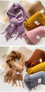 Detail der weichen Strickschal-Textur mit gedrehten Fransen und elegantem Marken-Patch