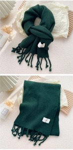 Detail eines dunkelgrünen Strickschals mit langen Fransen und minimalistischem egg-Label