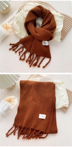 Details des karamellfarbenen Strickschals mit Fransen und minimalistischem Markenetikett