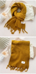 Detail eines senfgelben Strickschals mit weichen Fransen und dezentem Markenetikett