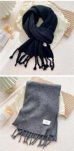 Detailansicht der gestrickten Winterschals in Schwarz und Grau mit weichen Fransen und Etiketten