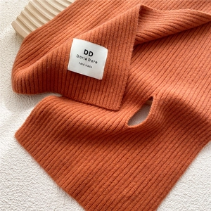 Close-up of bright orange knitted scarf with handmade fabric label and ribbed texture