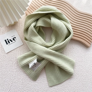 Detail shot of light green ribbed knit scarf with woven label on marble surface