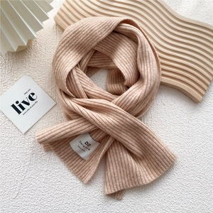 Detail of warm pink ribbed knit scarf featuring a white handmade brand label on texture