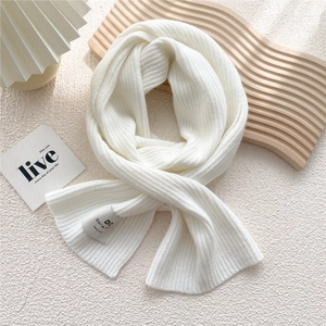 Detail of creamy white ribbed knit scarf featuring a gray handmade woven label