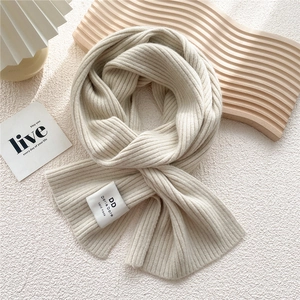 Detailed view of cream white knitted scarf with vertical ribs and handmade fabric label