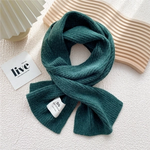 Macro shot of dark green ribbed-knit scarf texture with white woven label on white background