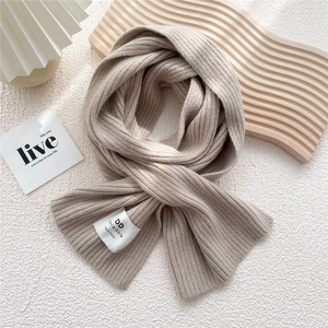 Detailed texture of beige ribbed knit scarf with a handmade woven brand label on surface