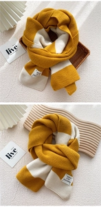 Detail of yellow and white striped knit scarf with decorative woven label on wooden board