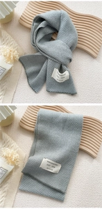 Detail of grey herringbone knit scarf with woven label on a textured background