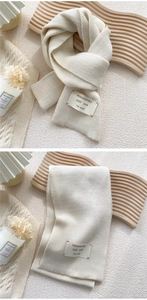 Detail of herringbone knit scarf in cream white with a minimalist fabric label