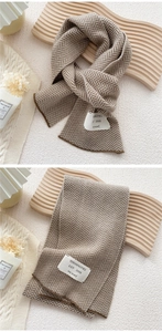 Detail view of brown herringbone knit scarf with woven fabric label and cozy texture