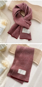 Detail of burgundy and cream herringbone knit scarf with woven brand tag and soft texture