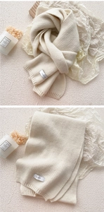 Detailed view of cream-white knitted scarf with brand label and thick warm texture