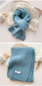 Close-up of thick light blue knit scarf texture and white FEIDING woven label detail