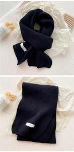 Close-up of thick black knitted scarf showing ribbed texture and white branded label